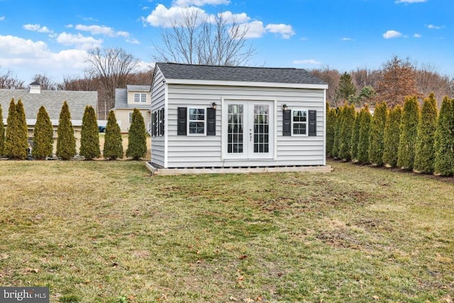 rear view of property featuring an outdoor structure, a yard, french doors, and a shingled roof