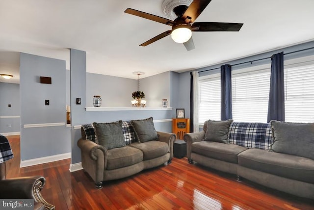 living area with ceiling fan with notable chandelier, baseboards, and hardwood / wood-style flooring