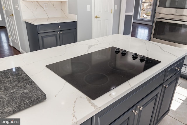 kitchen with light stone counters, backsplash, gray cabinetry, and black electric cooktop