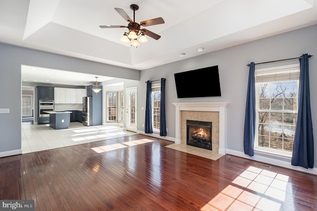 unfurnished living room with light wood finished floors, visible vents, baseboards, and a tray ceiling