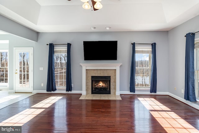 unfurnished living room featuring ceiling fan, baseboards, a fireplace, a raised ceiling, and wood-type flooring