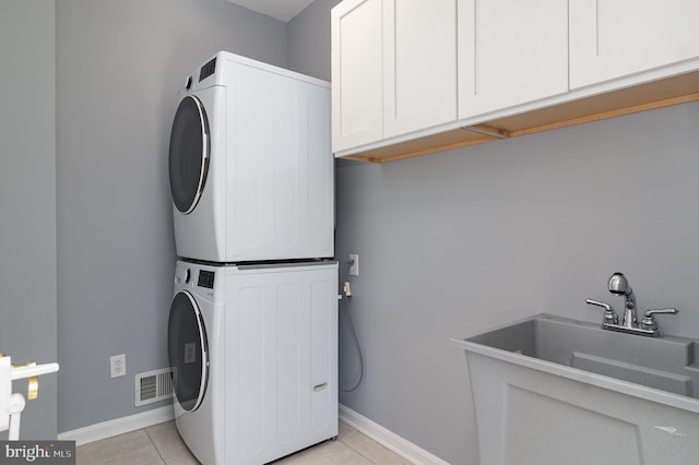 washroom with light tile patterned floors, stacked washer / drying machine, cabinet space, and visible vents