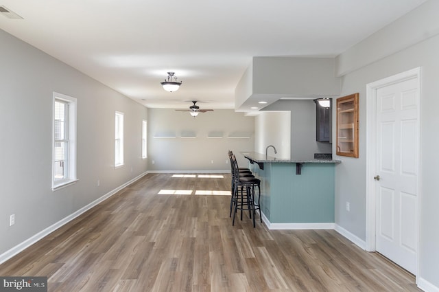 kitchen with visible vents, baseboards, a breakfast bar, stone counters, and wood finished floors