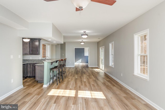 kitchen with light wood-type flooring, a kitchen bar, baseboards, and dark brown cabinetry