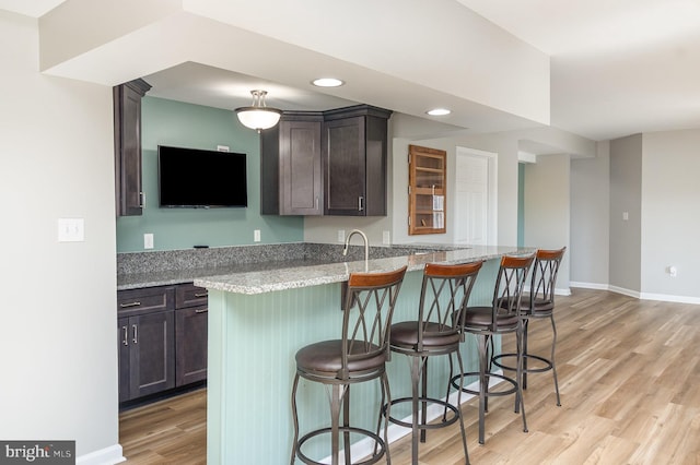 kitchen featuring a breakfast bar area, light stone countertops, baseboards, dark brown cabinets, and light wood-style floors