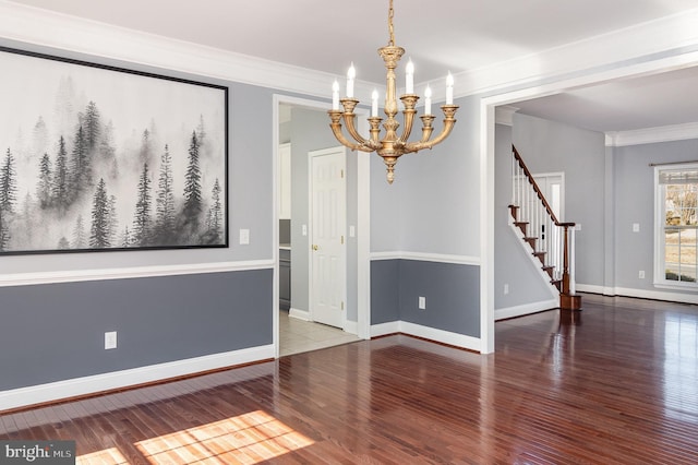 spare room featuring stairs, crown molding, wood finished floors, and a chandelier