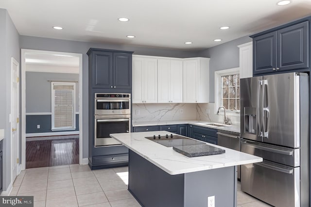 kitchen featuring a sink, tasteful backsplash, a center island, appliances with stainless steel finishes, and light tile patterned floors