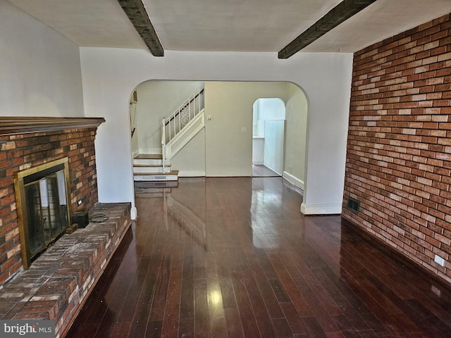 unfurnished living room featuring beam ceiling, hardwood / wood-style floors, arched walkways, brick wall, and a fireplace