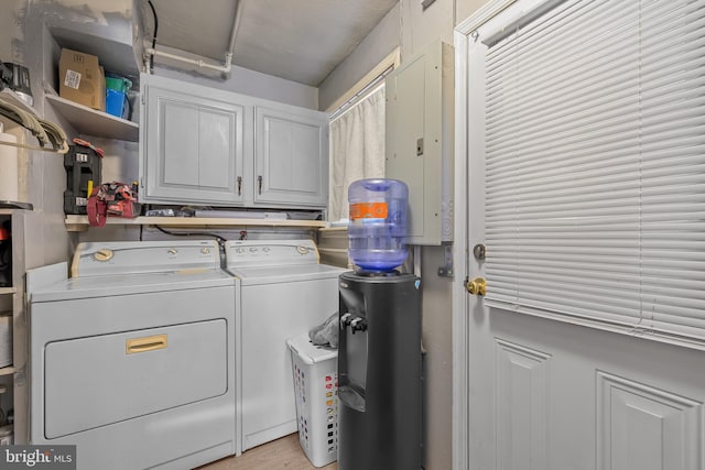 clothes washing area with electric panel, washer and dryer, and cabinet space