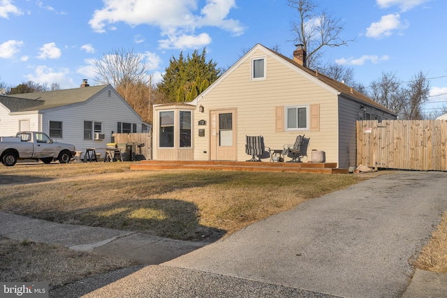 bungalow-style home featuring a front yard, a wooden deck, fence, and a chimney