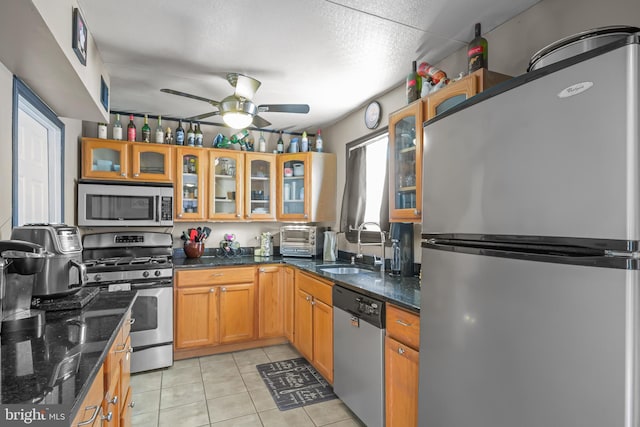 kitchen featuring a ceiling fan, a sink, stainless steel appliances, dark stone counters, and light tile patterned floors