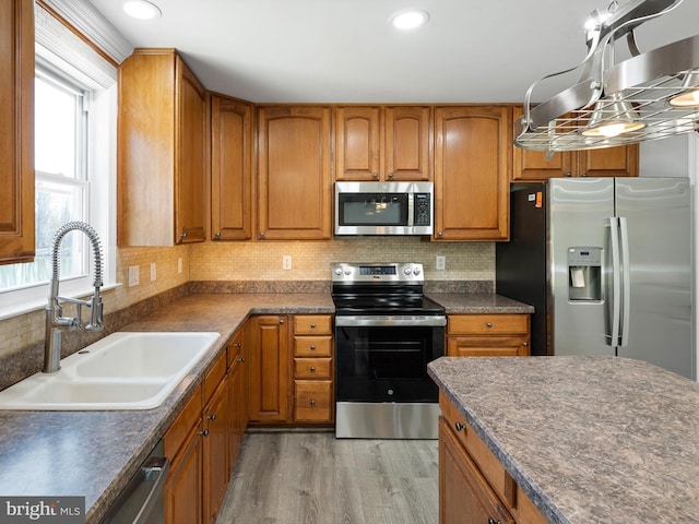 kitchen with brown cabinetry, light wood-style flooring, a sink, appliances with stainless steel finishes, and dark countertops