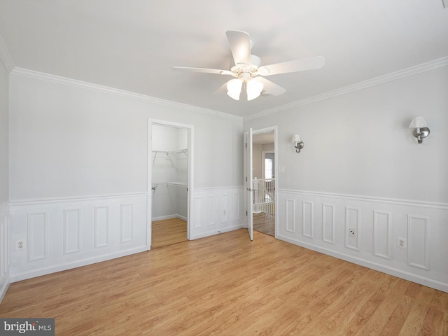 unfurnished bedroom with a spacious closet, crown molding, light wood-type flooring, and a closet