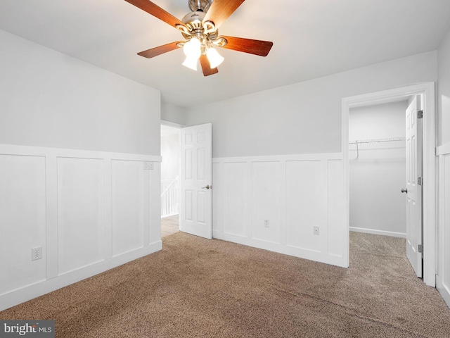 unfurnished bedroom with a walk in closet, ceiling fan, carpet, a closet, and a decorative wall