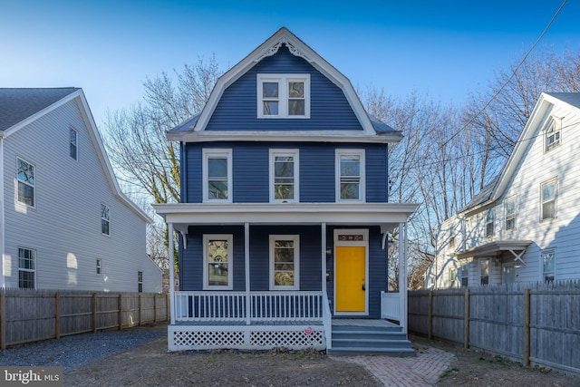 view of front of home featuring fence, covered porch, and a gambrel roof