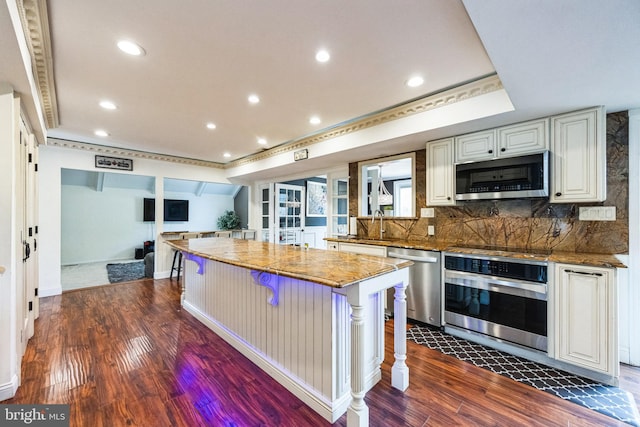 kitchen with tasteful backsplash, a center island, stone counters, stainless steel appliances, and dark wood-style flooring