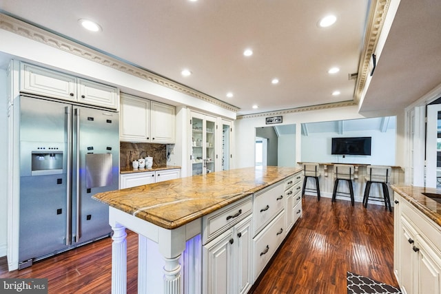 kitchen featuring light stone counters, built in refrigerator, dark wood-type flooring, and white cabinets