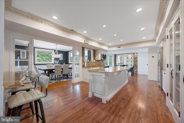 kitchen featuring a tray ceiling, dark wood-type flooring, ornamental molding, and a center island