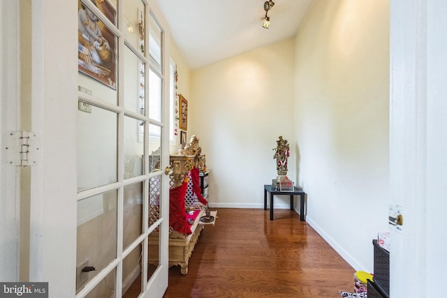 corridor featuring lofted ceiling, wood finished floors, and baseboards