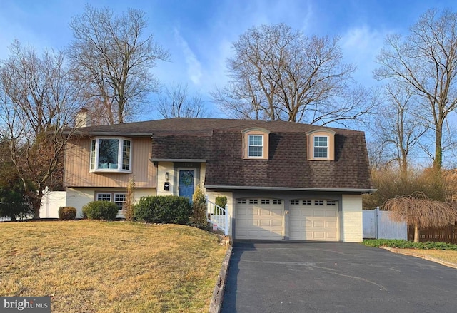 bi-level home featuring aphalt driveway, a front yard, roof with shingles, and fence