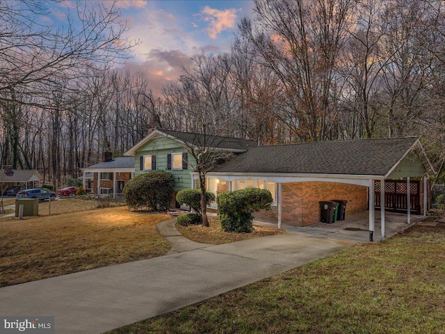 tri-level home with brick siding, an attached carport, fence, concrete driveway, and a lawn