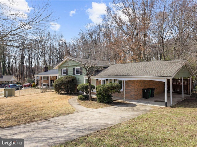 tri-level home featuring roof with shingles, concrete driveway, a front yard, a carport, and brick siding