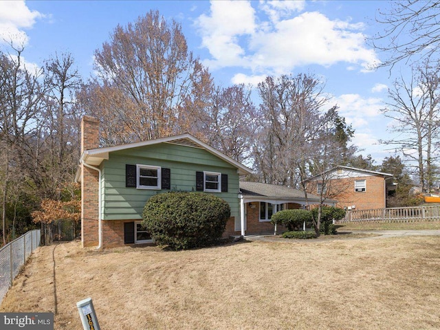 tri-level home with a front lawn, brick siding, a chimney, and fence