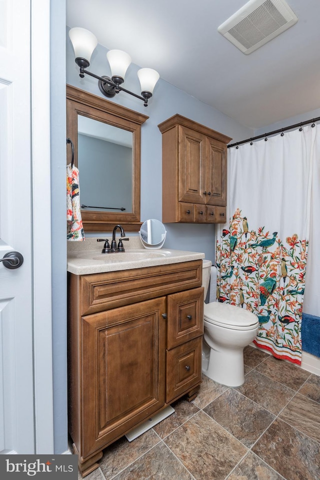 bathroom featuring vanity, a shower with shower curtain, visible vents, stone finish flooring, and toilet