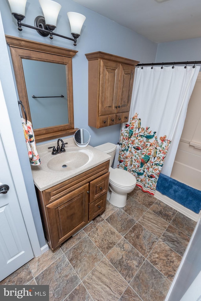 bathroom featuring toilet, curtained shower, vanity, and stone finish floor