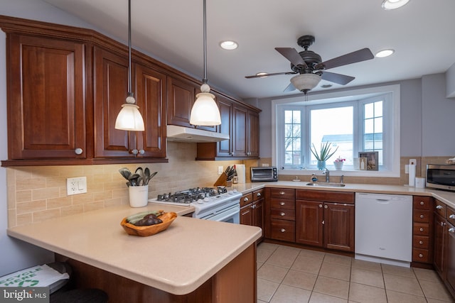 kitchen with white appliances, a peninsula, a sink, decorative backsplash, and under cabinet range hood