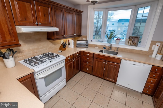 kitchen featuring white appliances, a sink, light countertops, under cabinet range hood, and backsplash