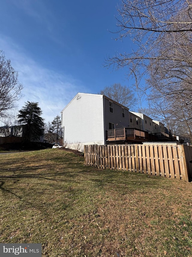 view of side of property with a yard, a wooden deck, and fence