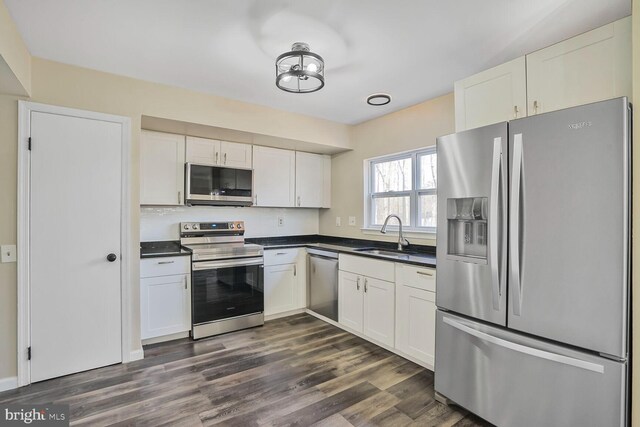 kitchen featuring dark wood-style floors, a sink, white cabinets, appliances with stainless steel finishes, and dark countertops