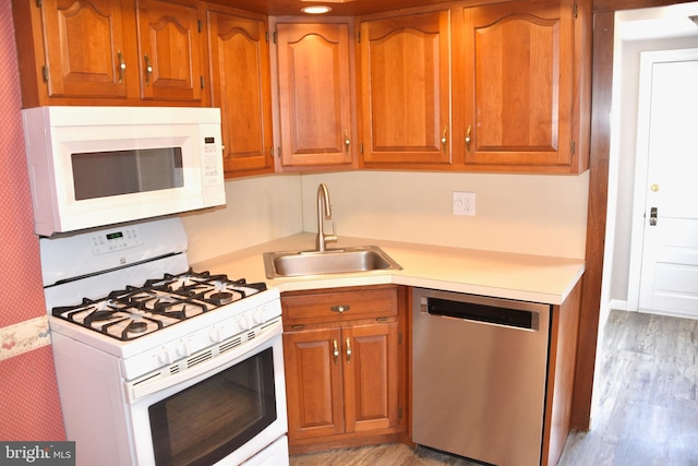 kitchen with brown cabinetry, white appliances, light countertops, and a sink