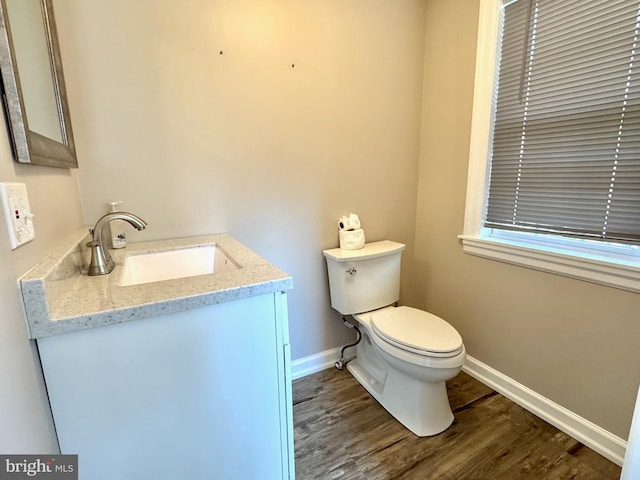 half bathroom featuring toilet, vanity, baseboards, and wood finished floors