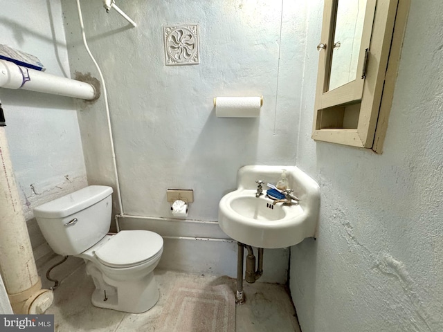 half bathroom featuring a sink, toilet, and a textured wall