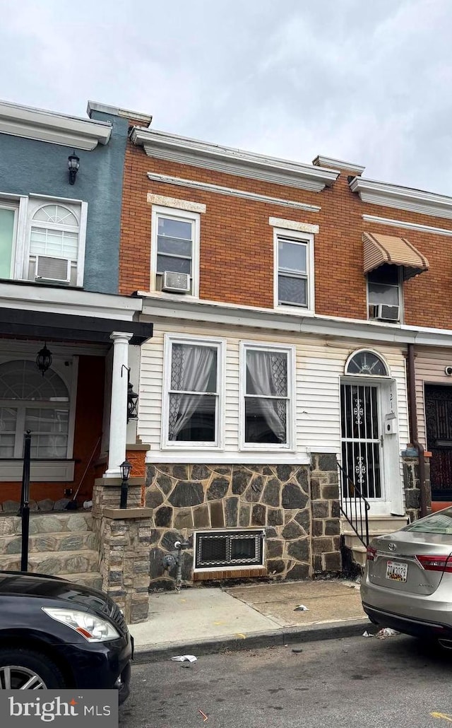 townhome / multi-family property featuring cooling unit, brick siding, and stone siding