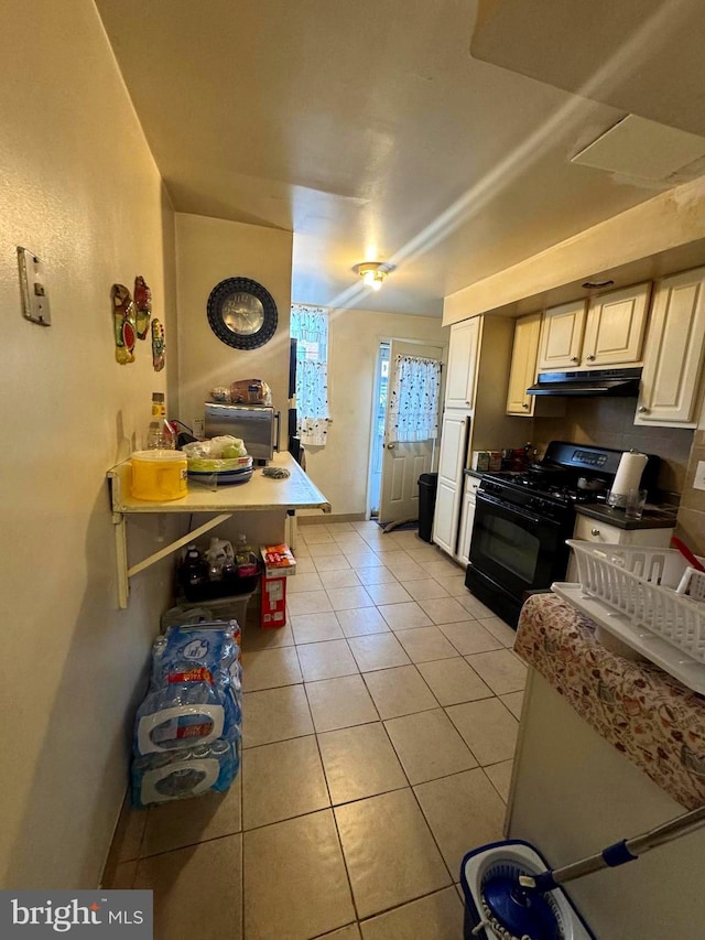 kitchen featuring under cabinet range hood, gas stove, and light tile patterned flooring