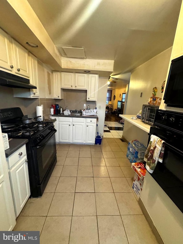 kitchen with black gas range, dark countertops, light tile patterned flooring, and white cabinets