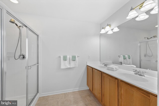 full bathroom with double vanity, a stall shower, baseboards, and a sink