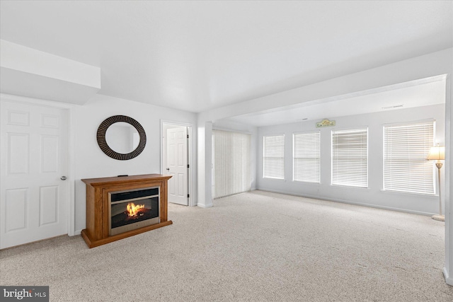 unfurnished living room featuring a glass covered fireplace, baseboards, and carpet floors