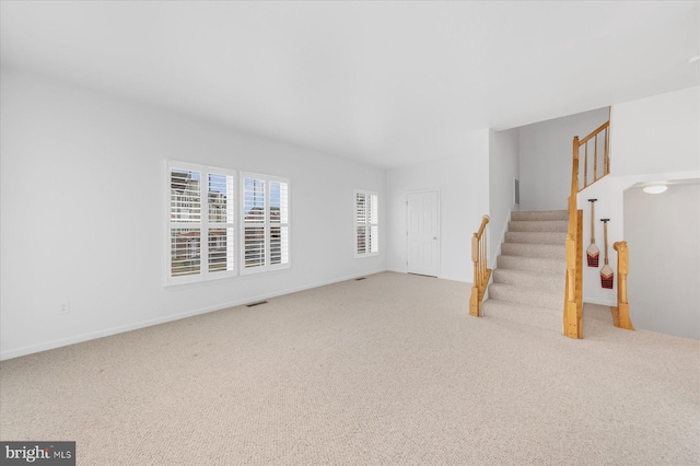 unfurnished living room featuring stairway, visible vents, and carpet