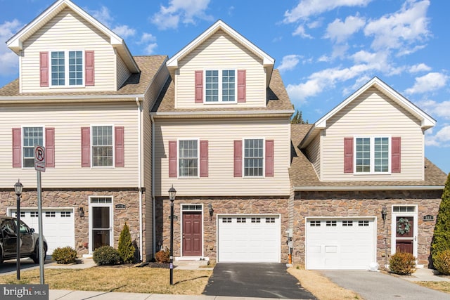 view of front of house with stone siding, driveway, a shingled roof, and an attached garage