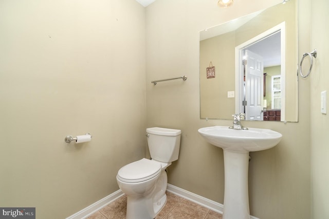 half bath featuring tile patterned flooring, toilet, baseboards, and a sink