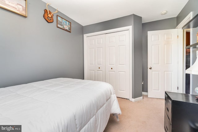 bedroom with a closet, light carpet, and baseboards