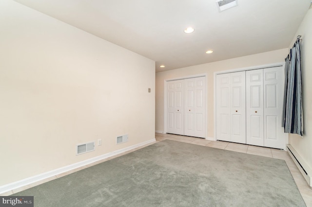 unfurnished bedroom with visible vents, two closets, and a baseboard radiator