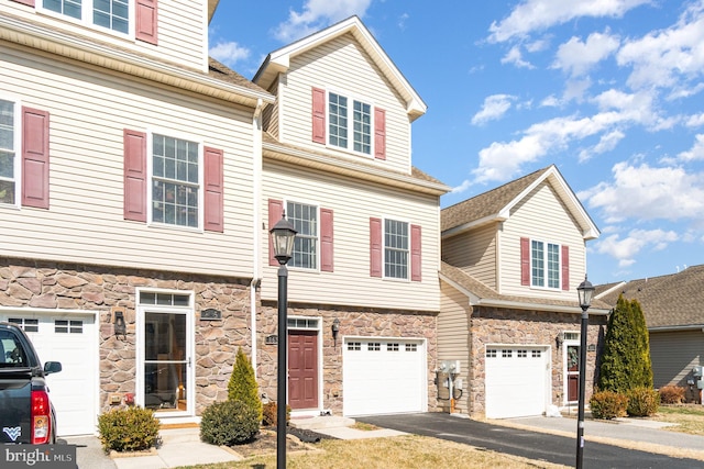 townhome / multi-family property with a garage, stone siding, and driveway