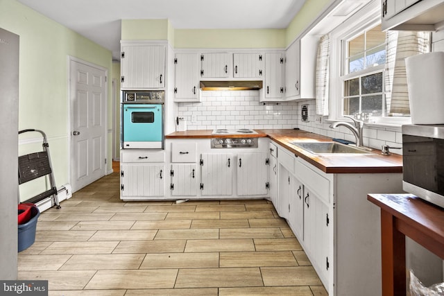 kitchen featuring stovetop, a sink, under cabinet range hood, wall oven, and white cabinetry