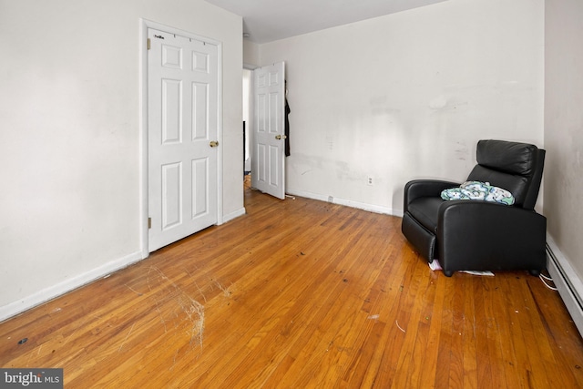 living area featuring baseboard heating, light wood-type flooring, and baseboards