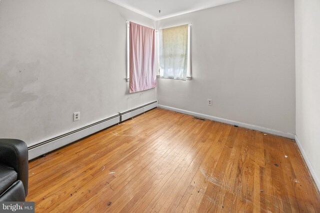 spare room featuring baseboards, wood-type flooring, and a baseboard radiator